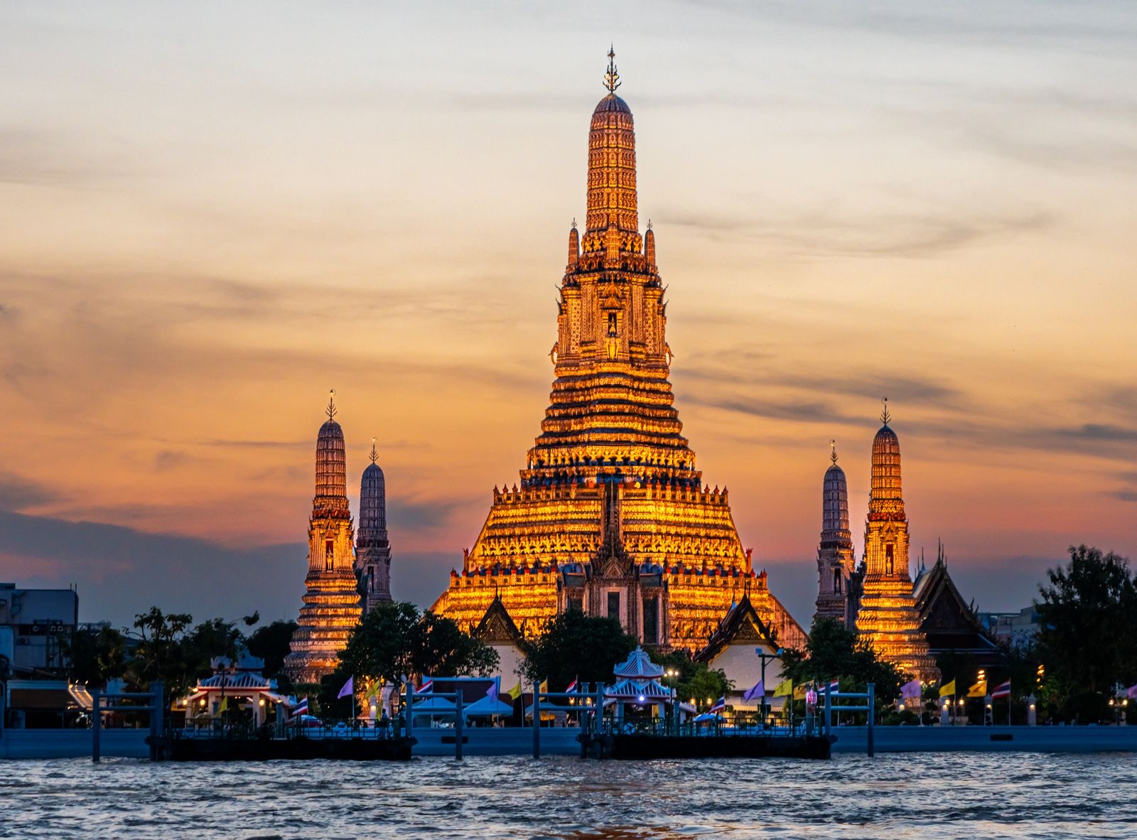 Le temple Wat Arun illuminé au coucher du soleil, au bord du fleuve à Bangkok